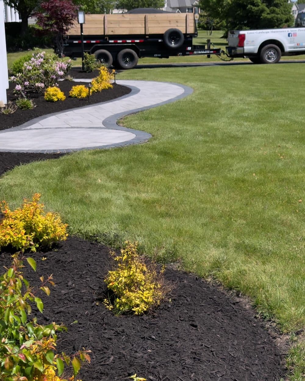 Curved stone pathway in landscaped yard with colorful flowers and a trailer in background.