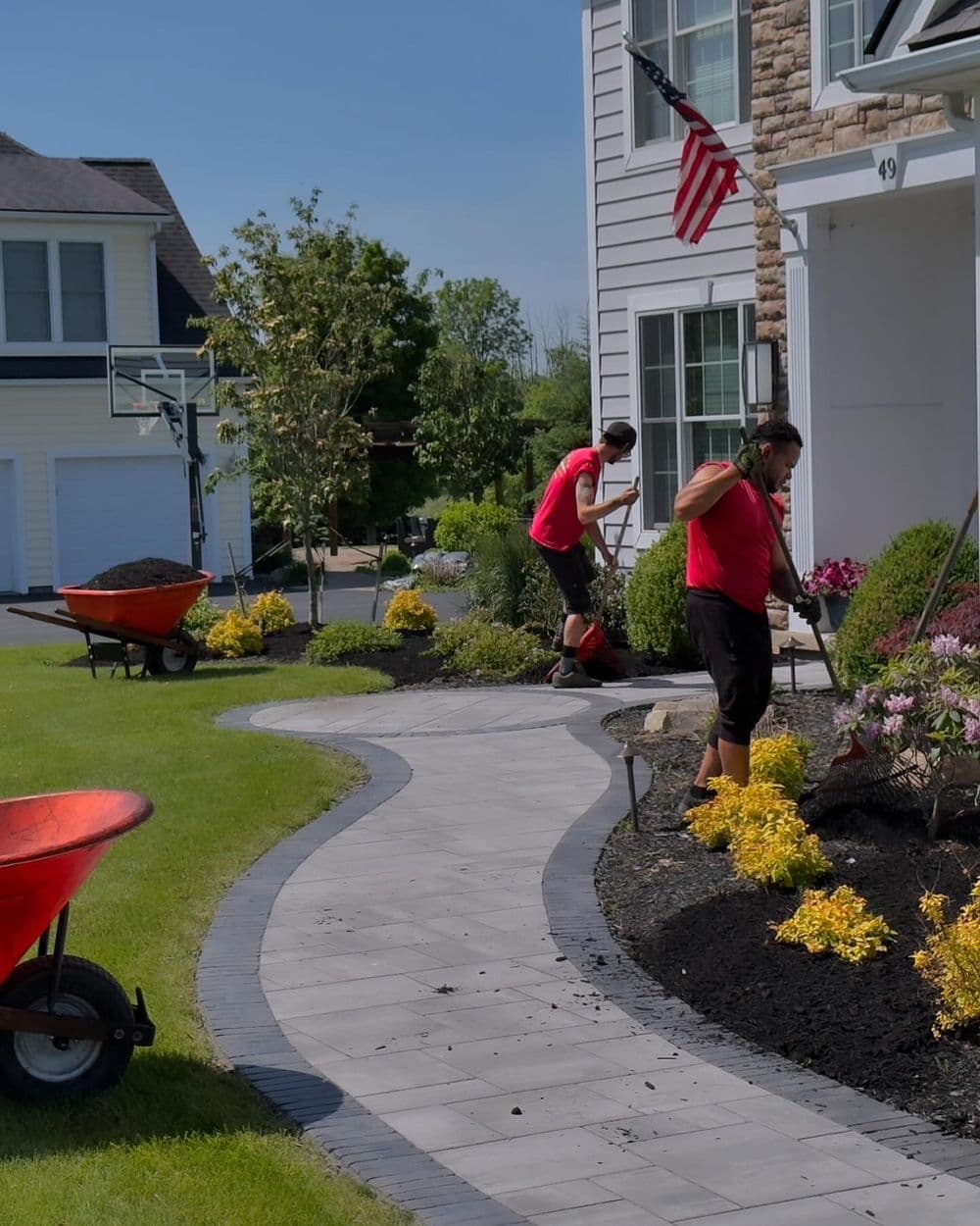 Landscapers working on garden beds with mulch and flowers in a residential yard.