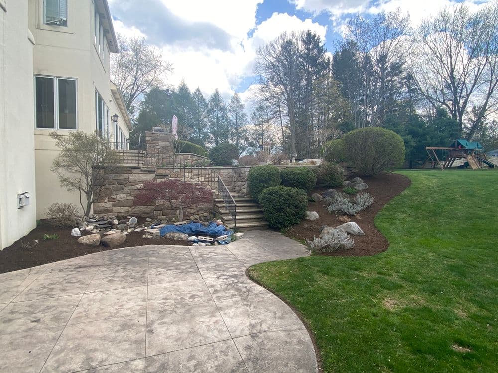 Backyard landscape with stone steps, shrubs, and a playset under a cloudy sky.