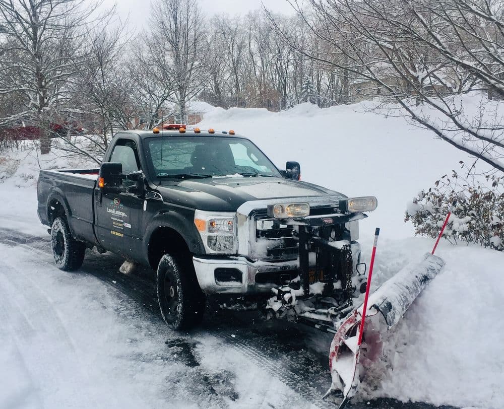 Snow plow truck clearing snow on a winter road with trees in the background.