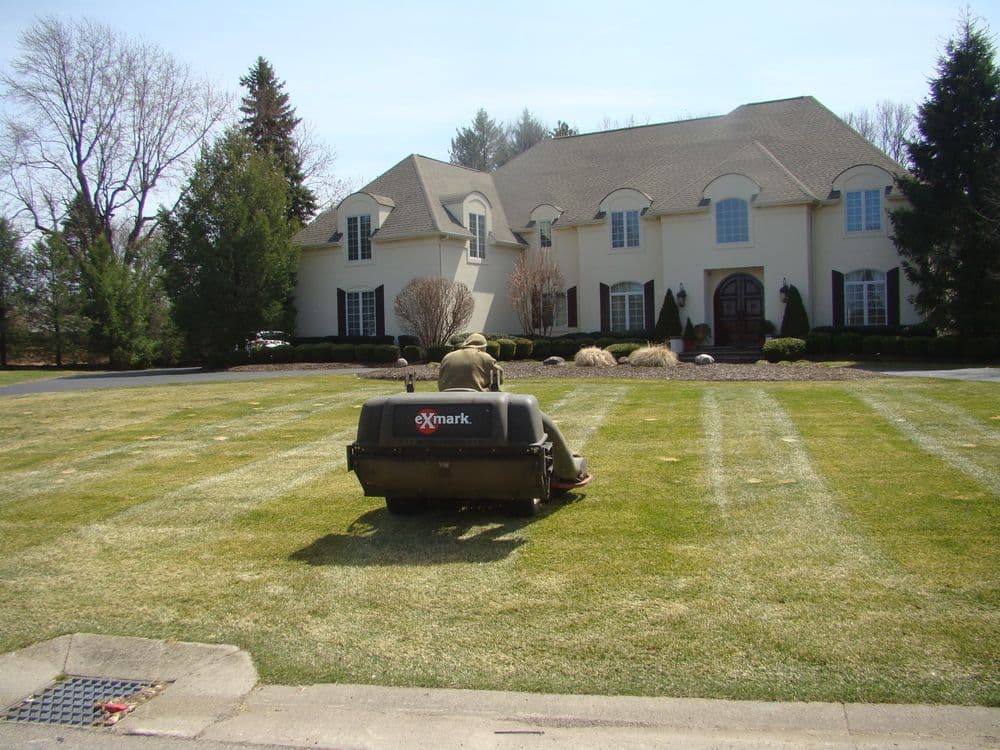Lawn care worker using Exmark mower on green lawn in front of a suburban home.