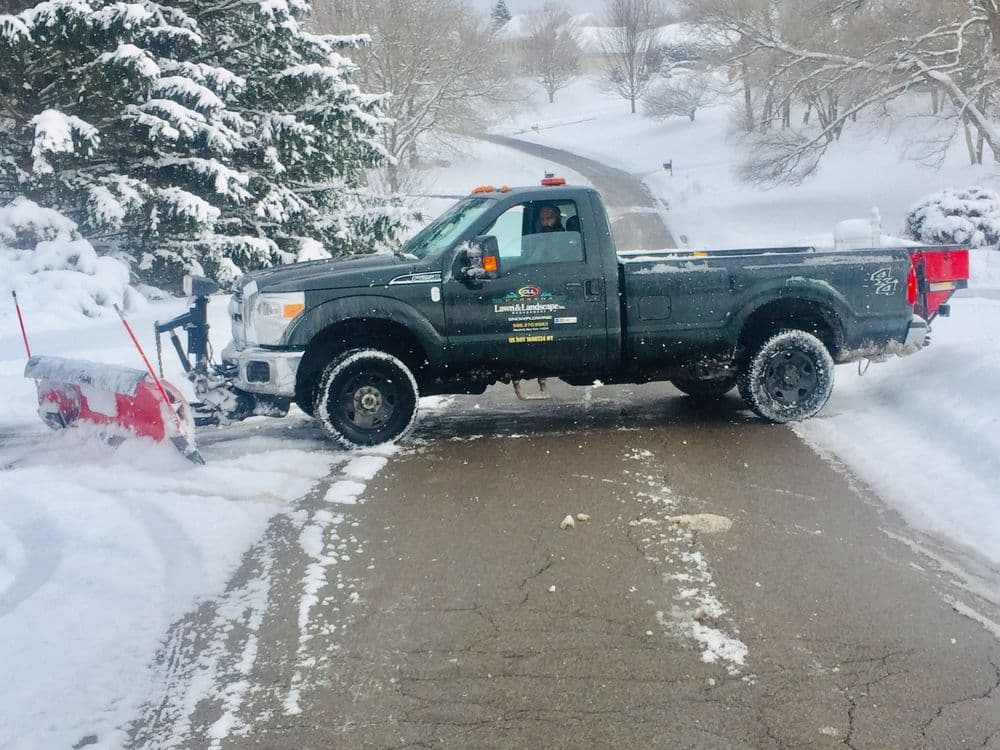 Snow plow truck clearing a residential road during winter snowstorm.