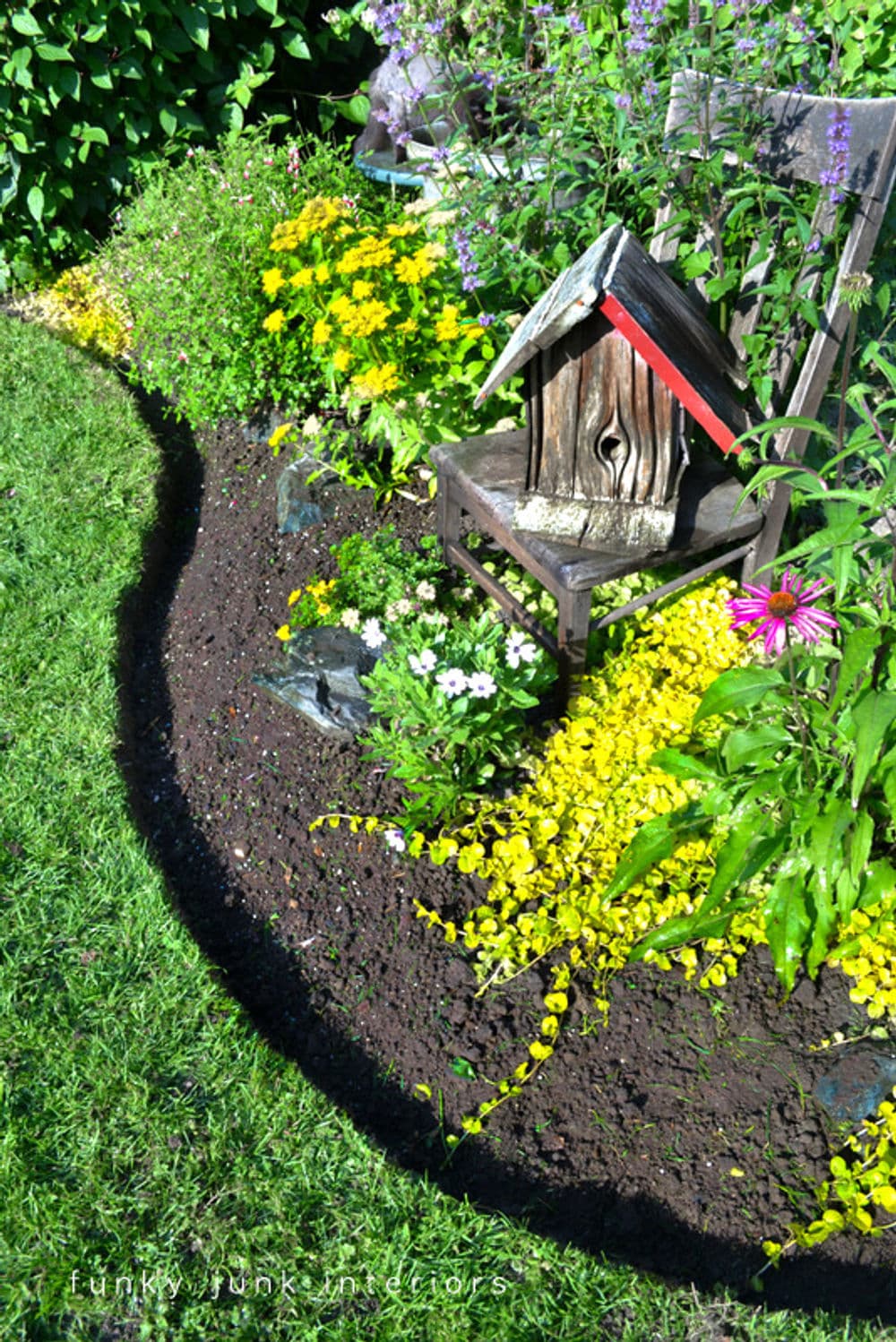 Colorful garden with flowers, a decorative birdhouse, and a curved flowerbed edge.