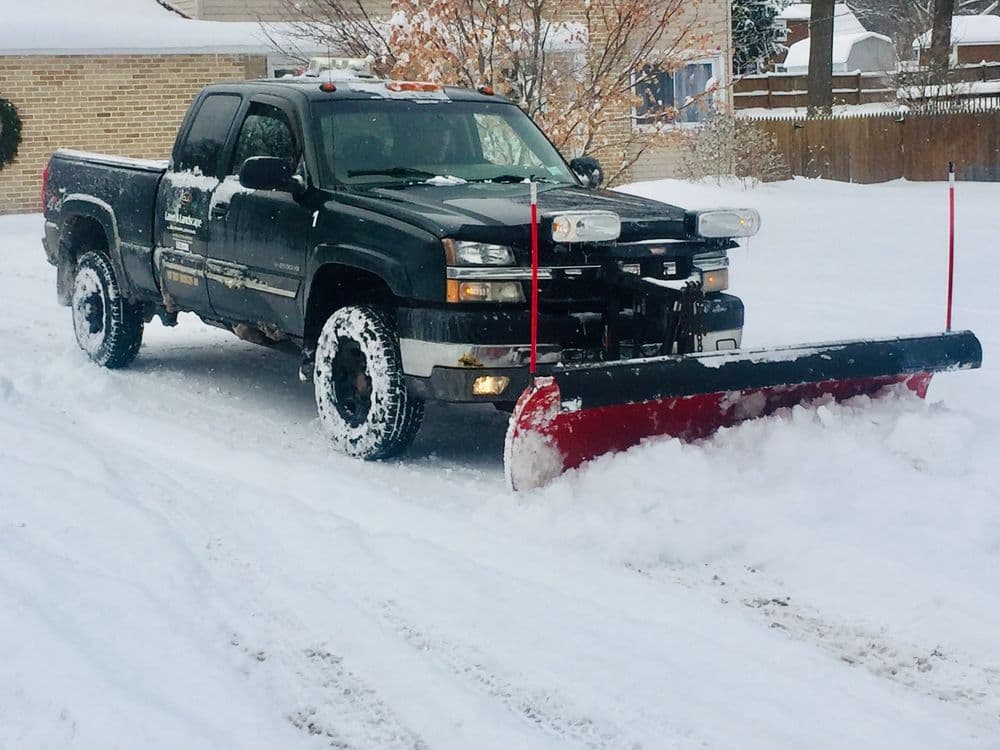 Black pickup truck with snow plow clearing snow on residential street.