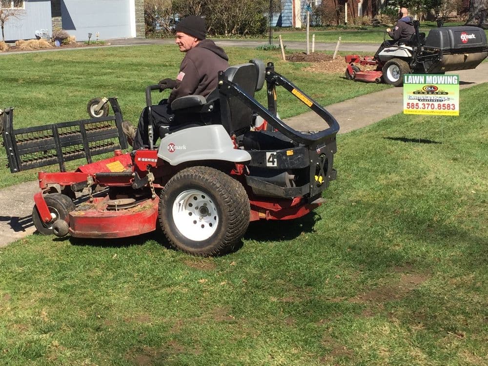 Lawn care professional mowing grass on a zero-turn mower in a residential yard.
