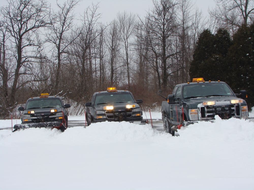Three snow plows parked in a snowy landscape, ready for winter road clearing.