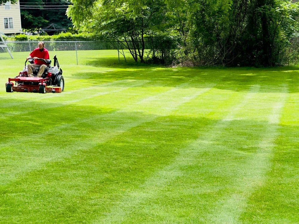 Man mowing a lush green lawn with a riding mower, creating clean stripes in the grass.